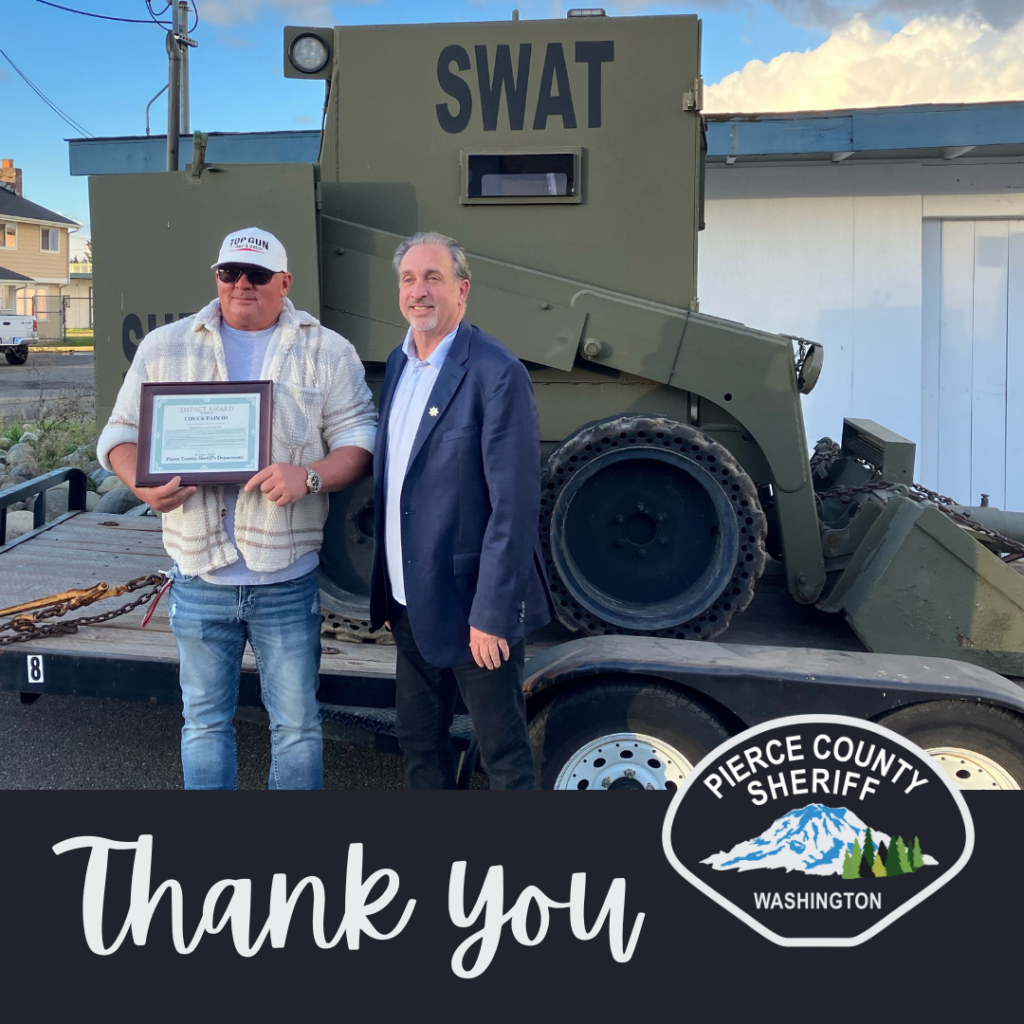 Sheriff Troyer hands Impact Award to Chuck Fain while they stand in front of the SWAT Team's armored vehicle